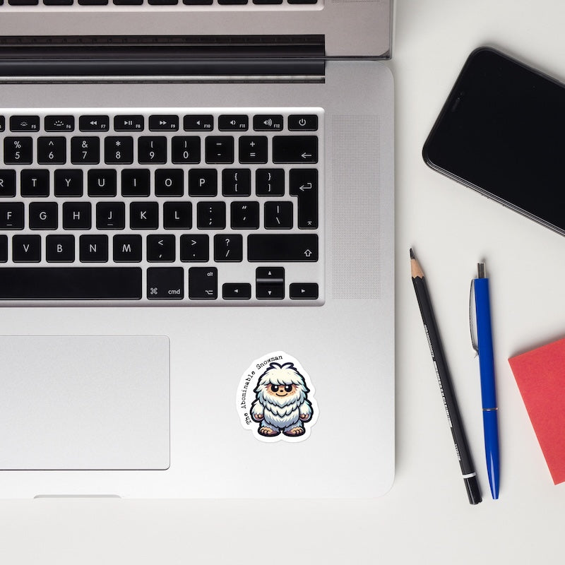 Laptop with a sticker of a cartoon character, phone, pencil, pen, and notebook on a white surface