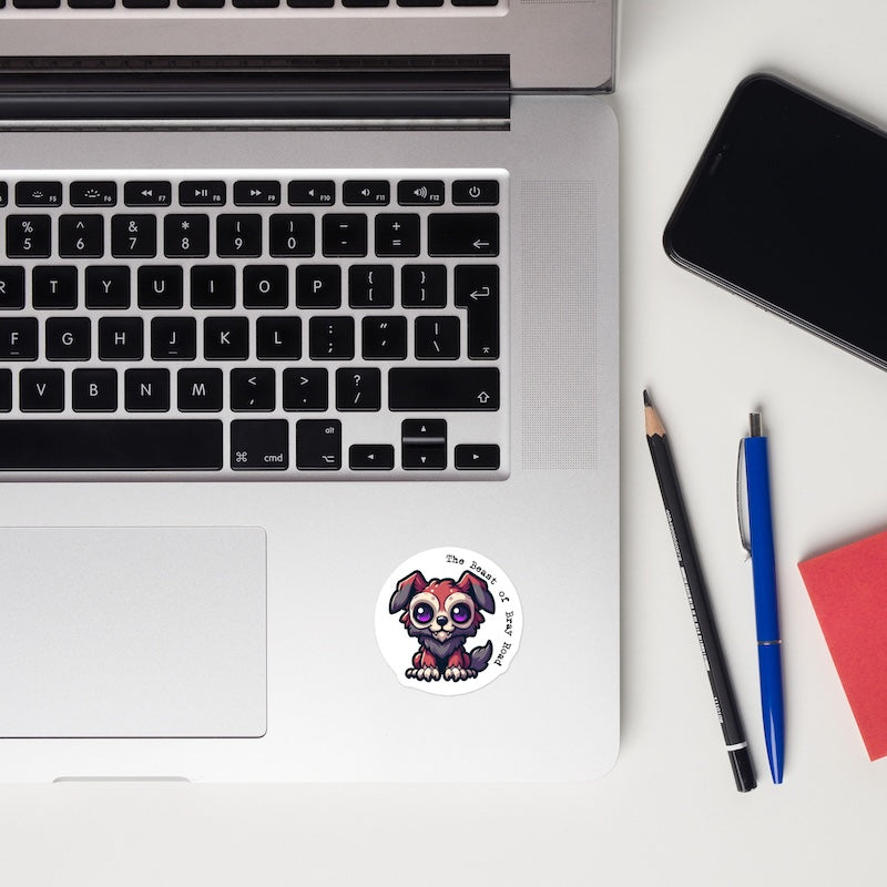 Laptop with a sticker of a cartoon dog, a phone, pencil, pen, and notebook on a white surface.