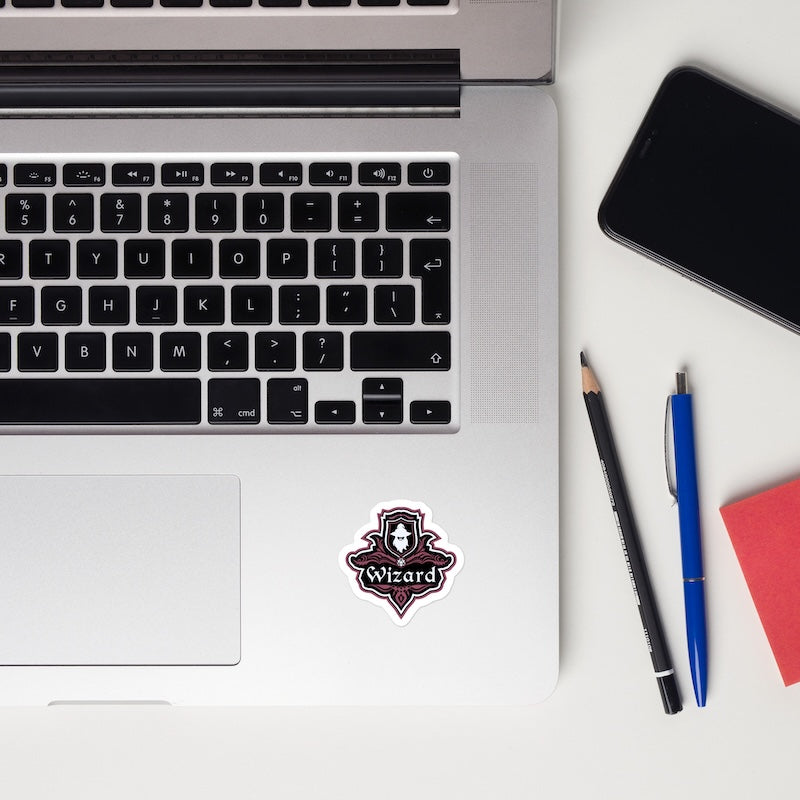 Laptop with 'Wizard' sticker, phone, pencil, pen, and notebook on a white surface