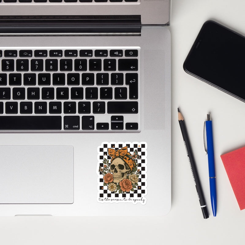 Laptop with a decorative sticker on a desk with a phone, pencils, and a notebook.