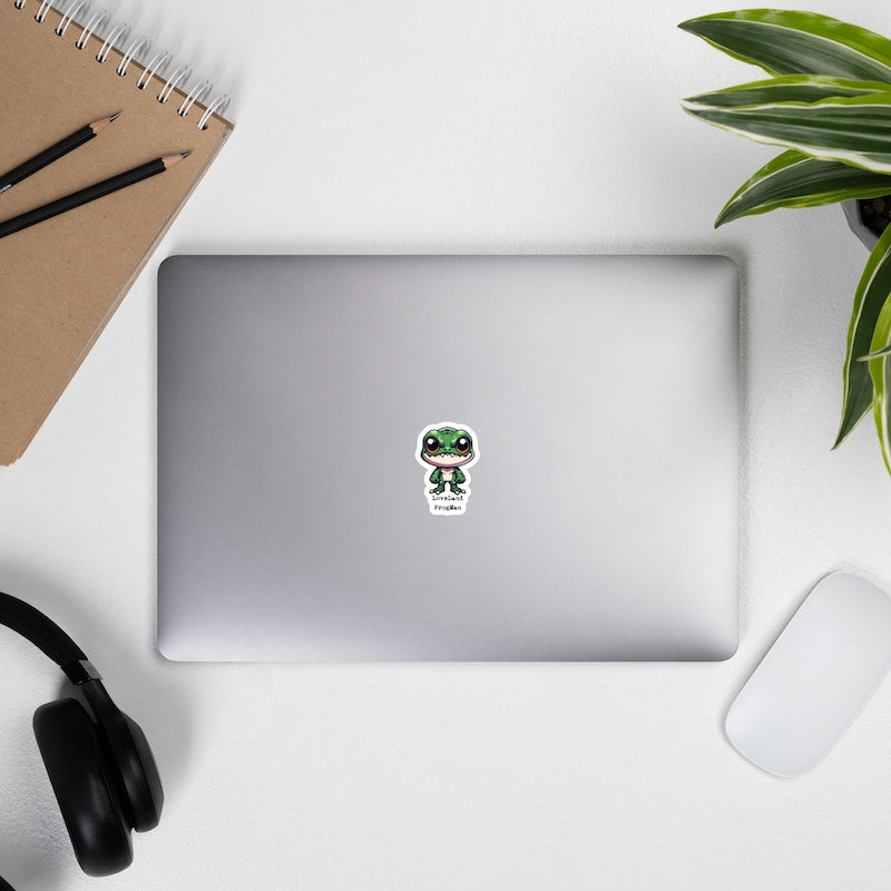 Laptop with a sticker on a desk with a notebook, pens, headphones, and a plant.