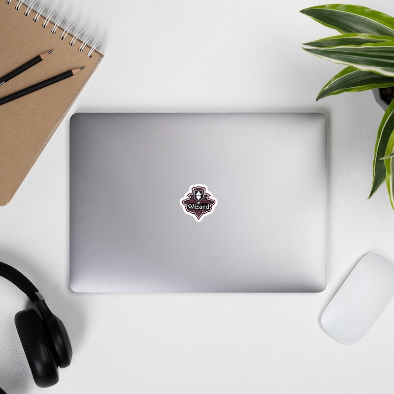 Laptop with a sticker on a desk with a notebook, pencils, headphones, and a plant.