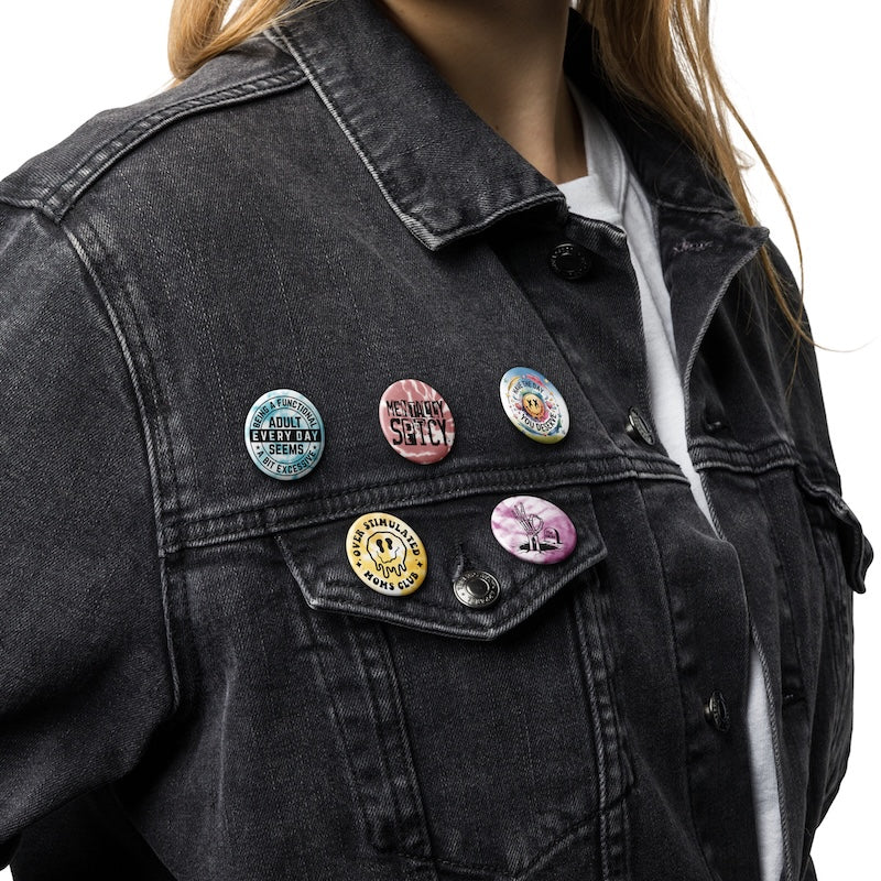 Person wearing a black denim jacket with various colorful pins on a white background