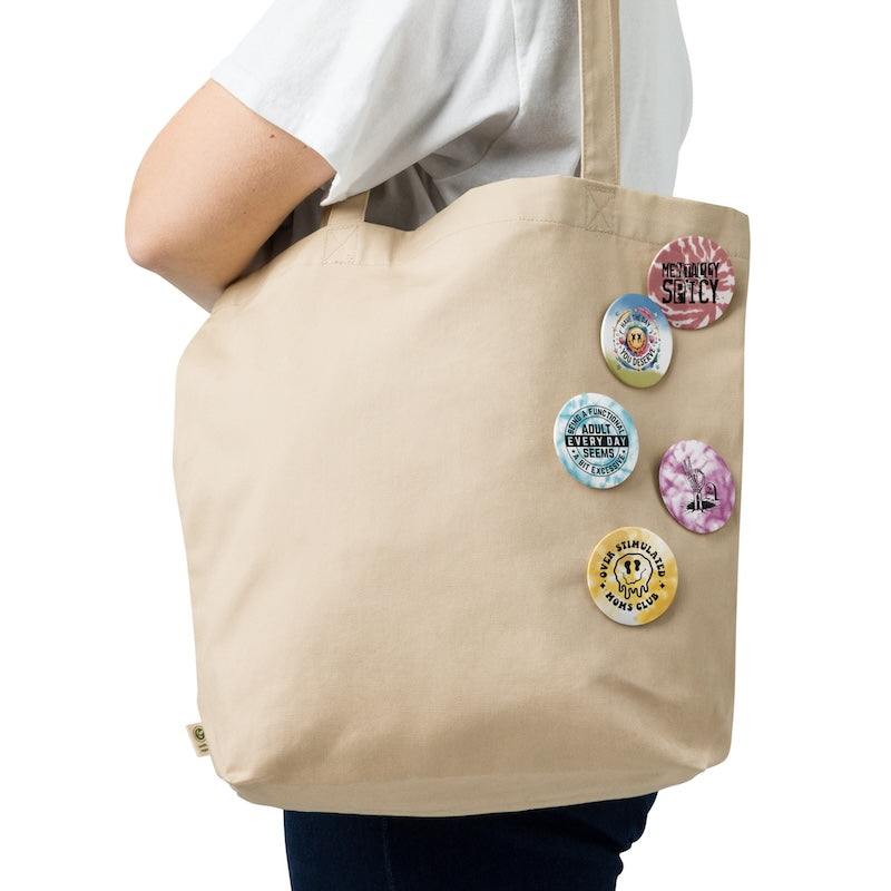 Beige tote bag with colorful buttons held by a person on a white background