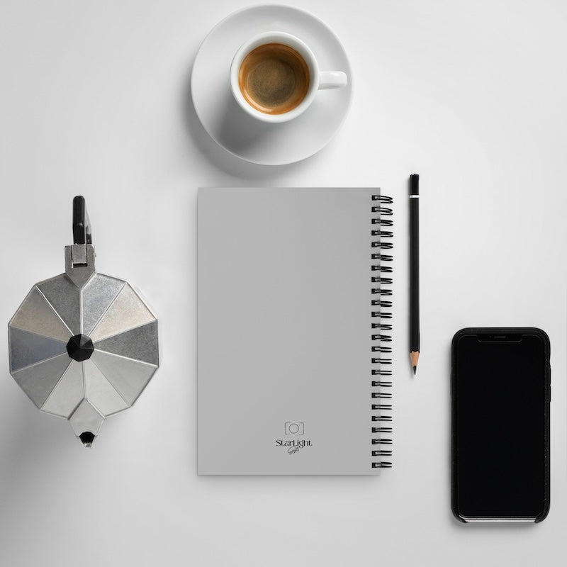 Flat lay of a notebook, coffee cup, smartphone, and small metallic device on a light gray background