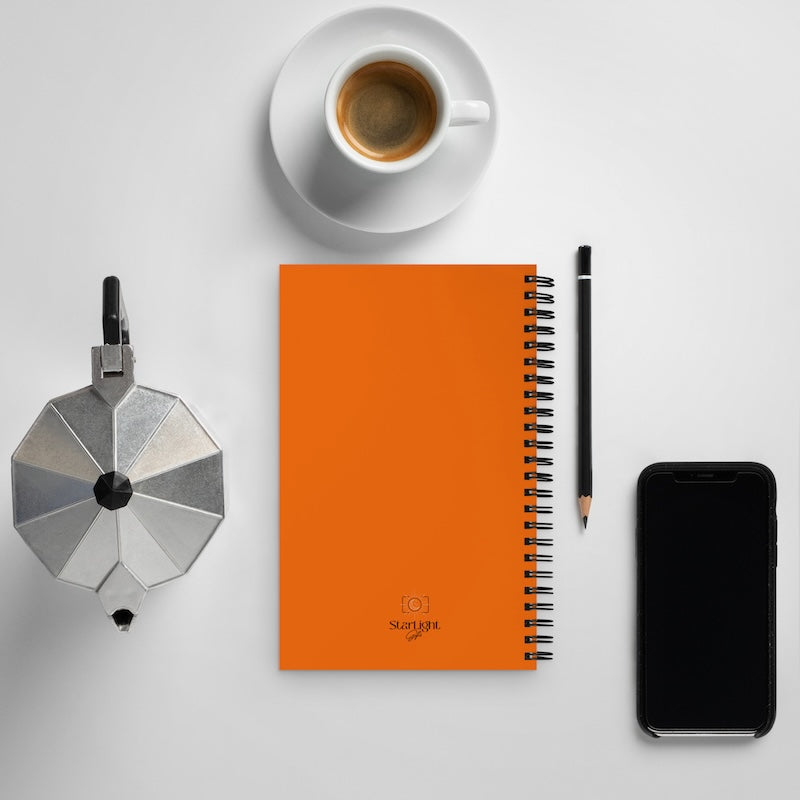 Orange notebook with a pen, coffee cup, and smartphone on a light gray background