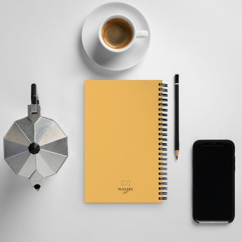 Yellow notebook with a pen, smartphone, coffee cup, and metallic object on a light gray background