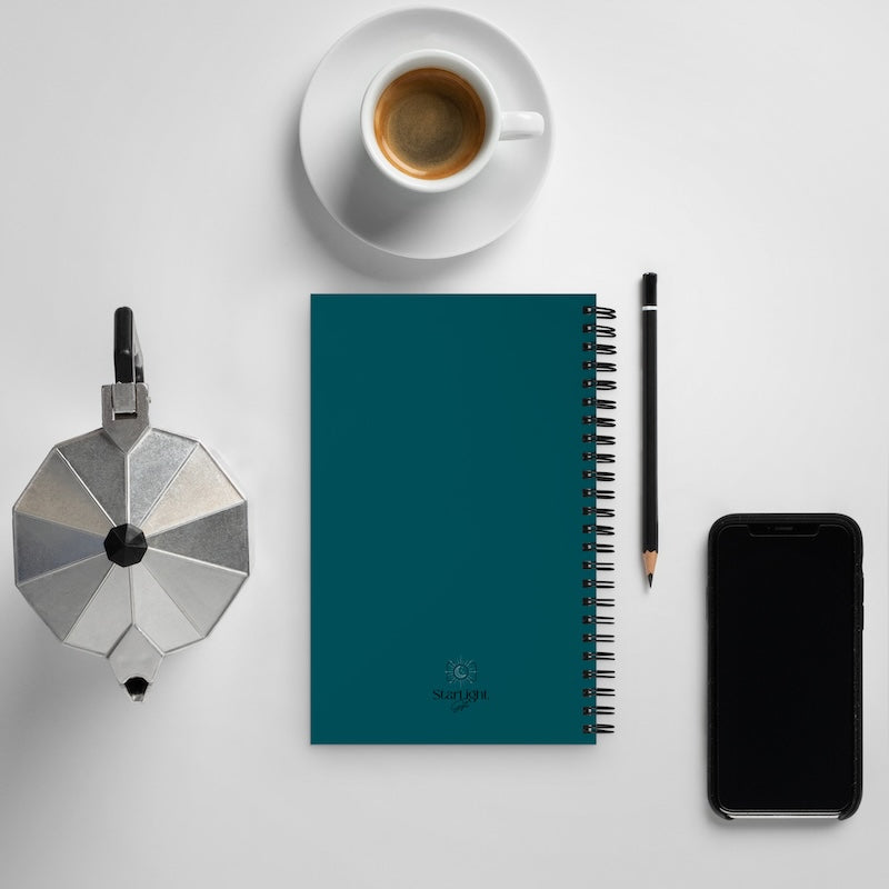 Teal notebook with a pen, smartphone, coffee cup, and small metallic object on a light gray background