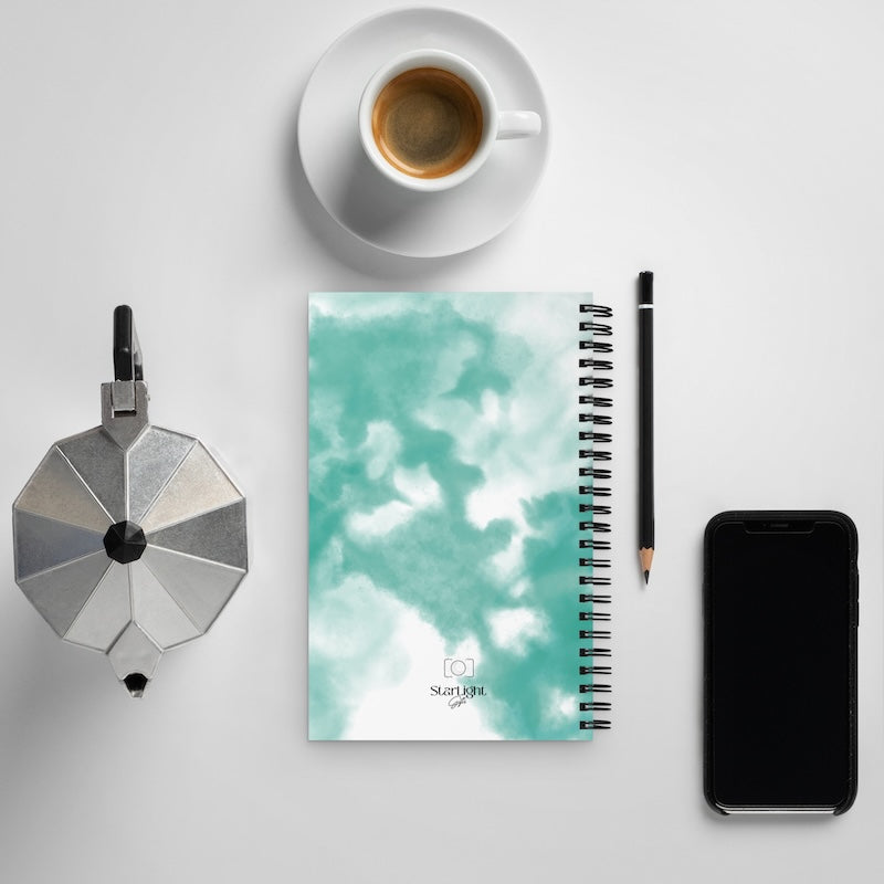Notebook with a cloud design, coffee cup, pencil, and phone on a light gray background