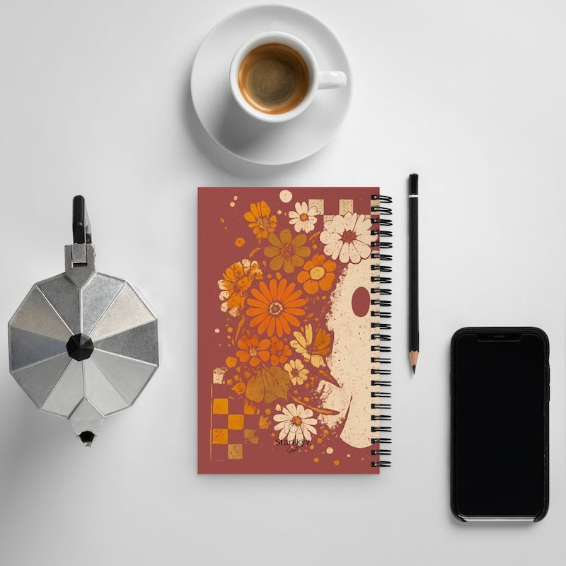 Notebook with floral design, coffee cup, pencil, and phone on a light gray background
