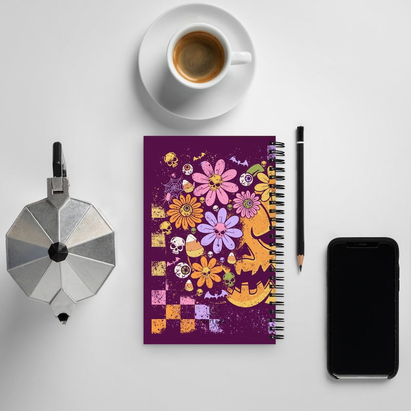 Notebook with colorful floral design on a white surface with a coffee cup, phone, and other items.