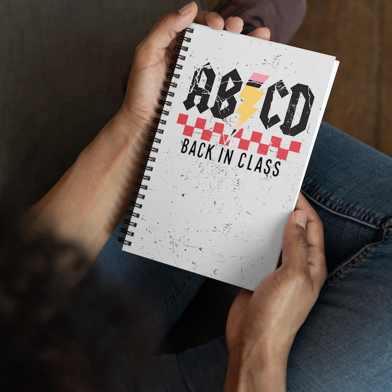 Person holding a notebook with 'AB/CD Back in Class' design