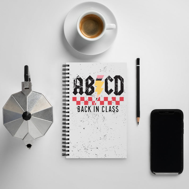Notebook with 'Back in Class' design, coffee cup, phone, and pencil on a light gray background