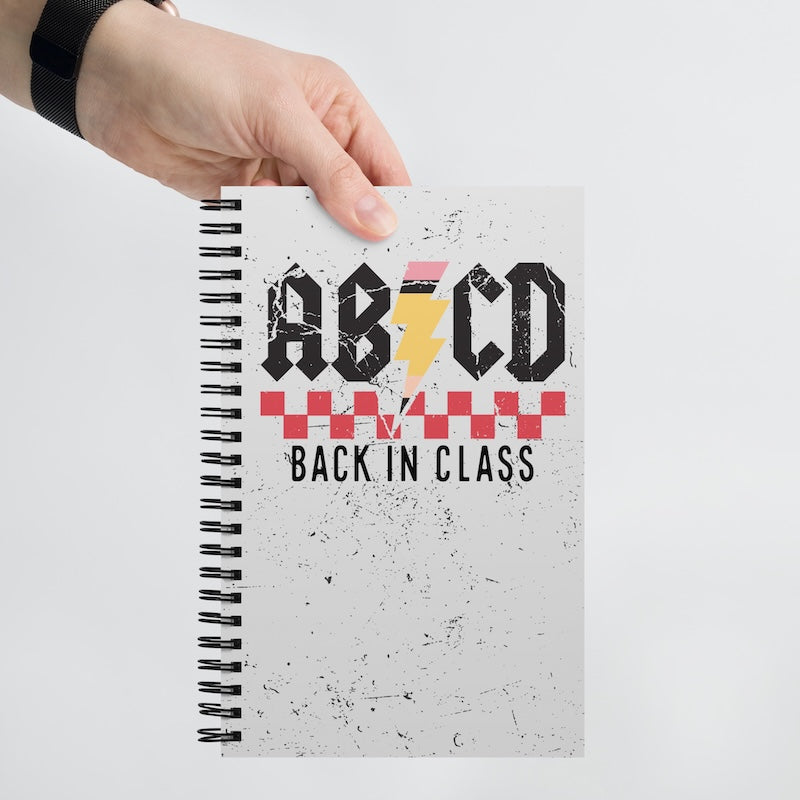 Notebook with 'ABCD Back in Class' design held by a hand on a light gray background