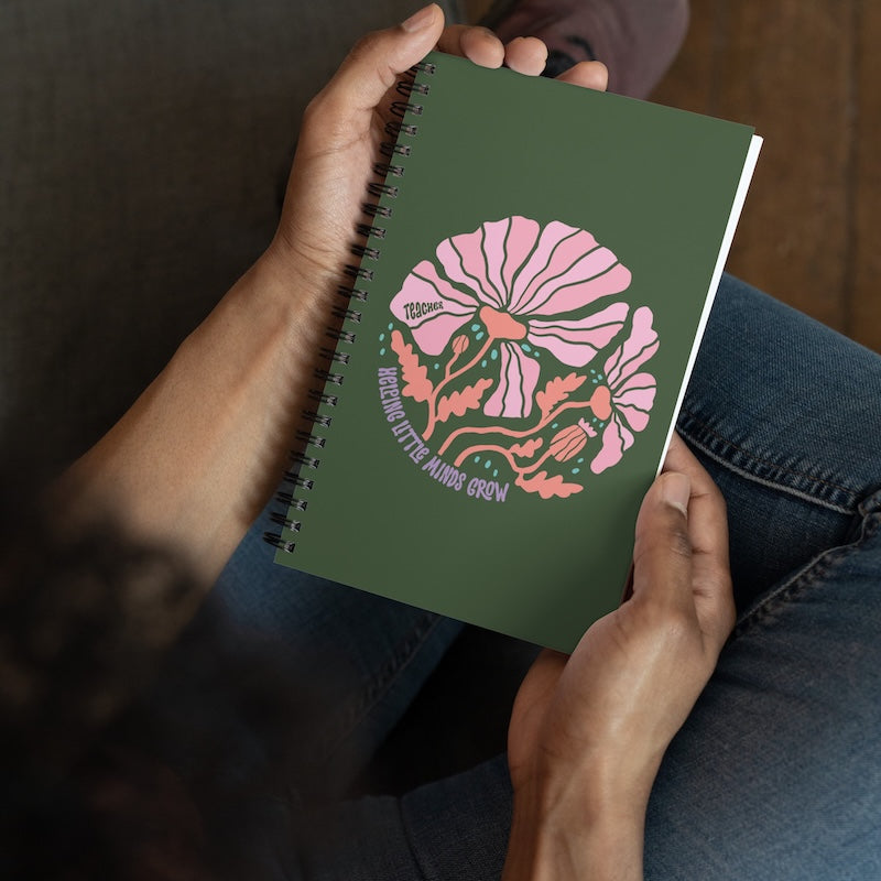 Green notebook with floral design held by a person wearing jeans.