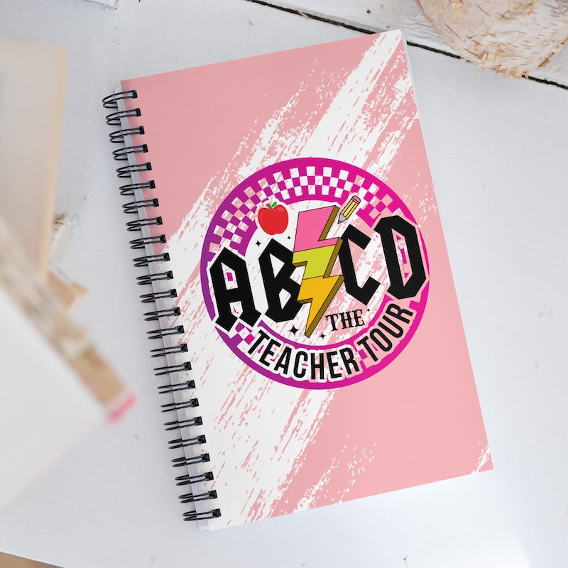 Notebook with 'ABCD The Teacher Tour' design on a white surface