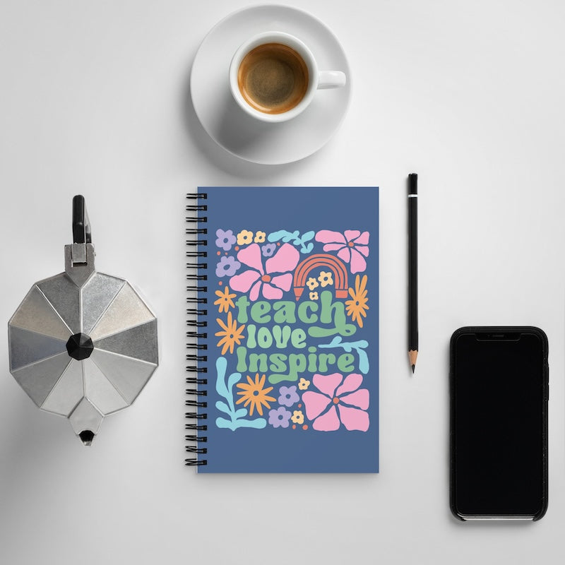 Notebook with floral design and text, coffee cup, phone, and pencil on a light gray background
