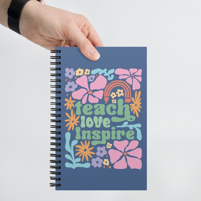 Notebook with 'teach love inspire' design held by a hand on a white background