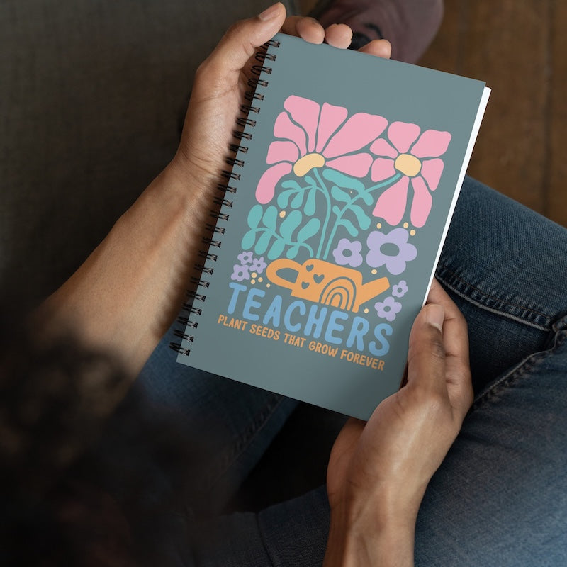 Notebook with floral design and 'Teachers' text held by hands
