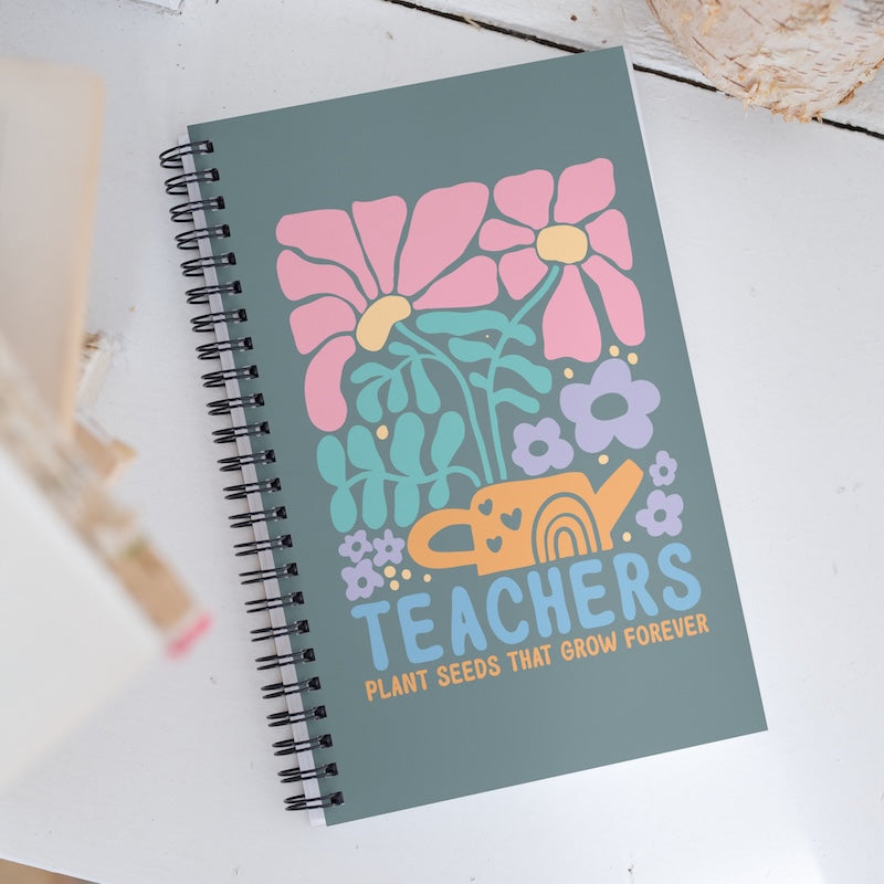 Notebook with floral design and 'Teachers Plant Seeds That Grow Forever' text on a white surface