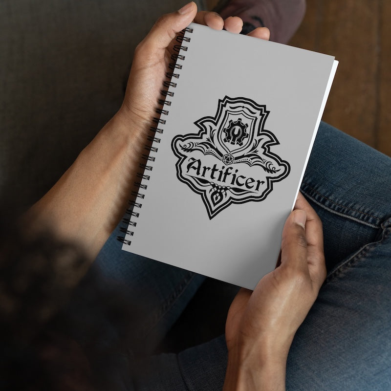 Person holding a notebook with 'Artificer' logo on a wooden surface