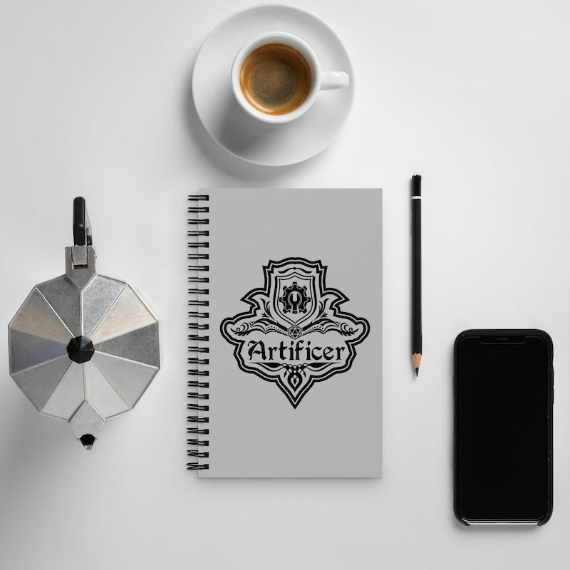 Notebook with 'Artificer' design, coffee cup, pen, and phone on a white surface