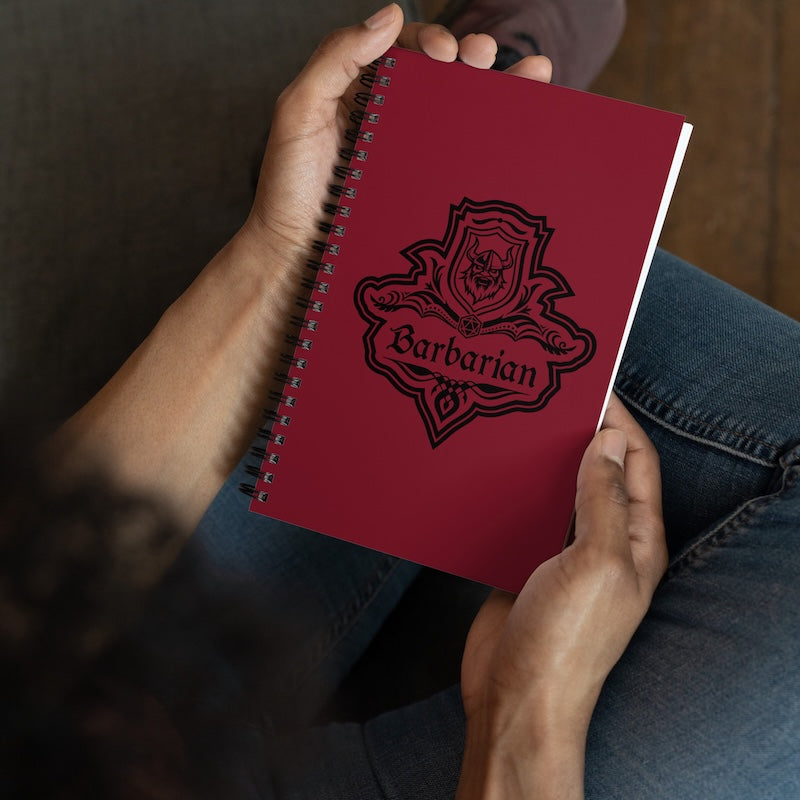 Red notebook with 'Barbarian' design held by a person wearing jeans.