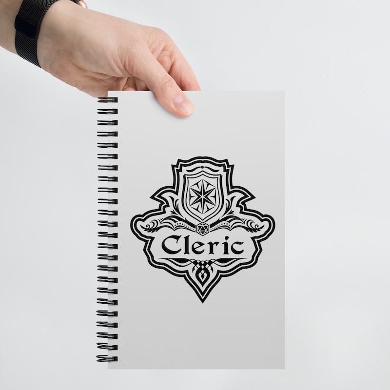 Notebook with 'Cleric' design held by a hand on a light gray background