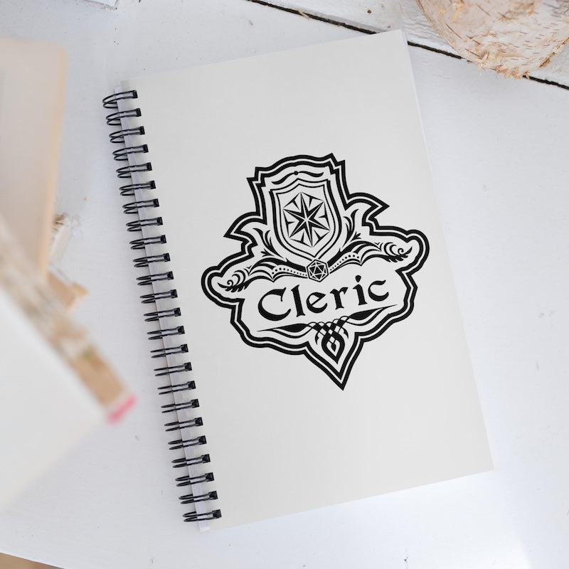 Black 'Cleric' emblem on a white notebook with a wooden surface in the background