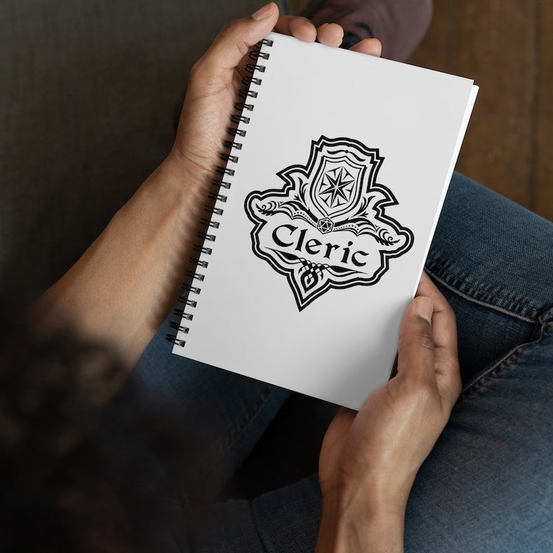 Person holding a notebook with 'Cleric' design on the cover