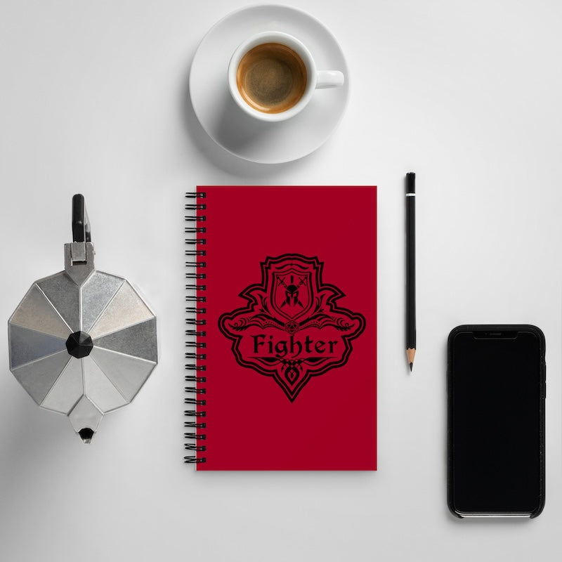 Red notebook with 'Fighter' emblem, coffee cup, phone, and pen on a light gray background
