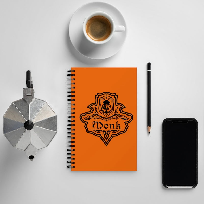 Orange notebook with 'Monk' design, coffee cup, pencil, and phone on a light gray background