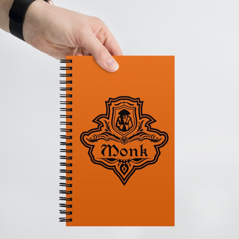 Orange notebook with 'Monk' design held by a hand on a light gray background