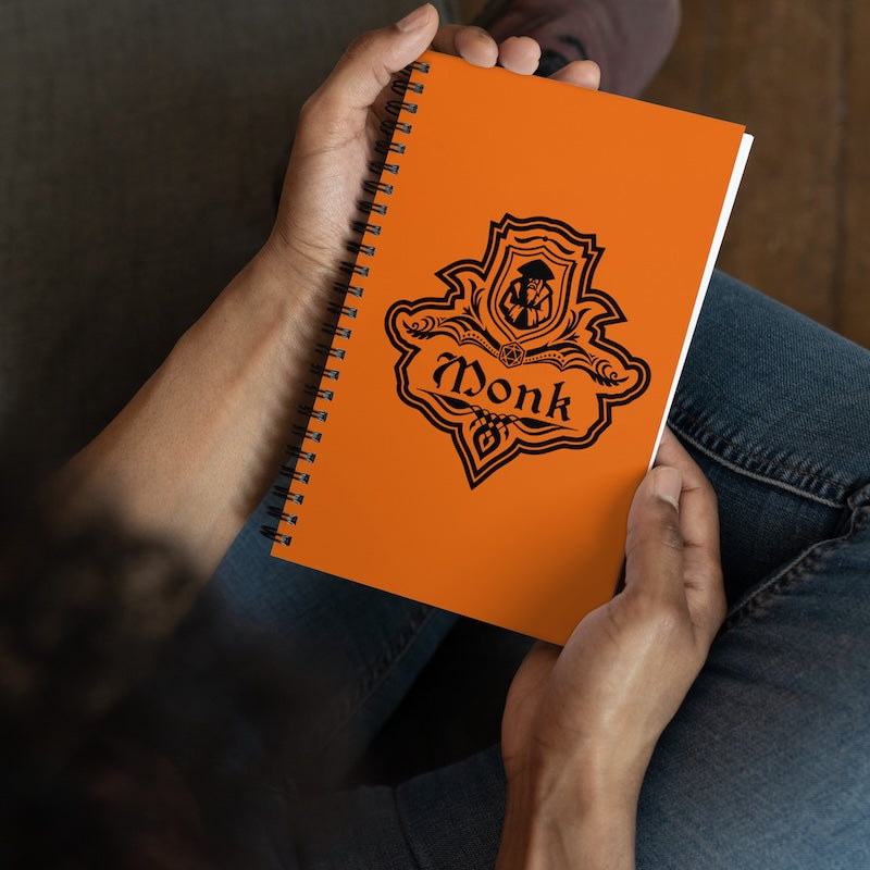 Orange notebook with a black emblem and 'Wonk' text held by hands against a dark background