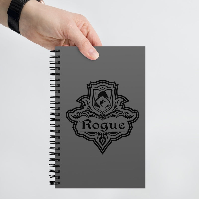 Gray notebook with 'Rogue' emblem held by a hand on a light gray background