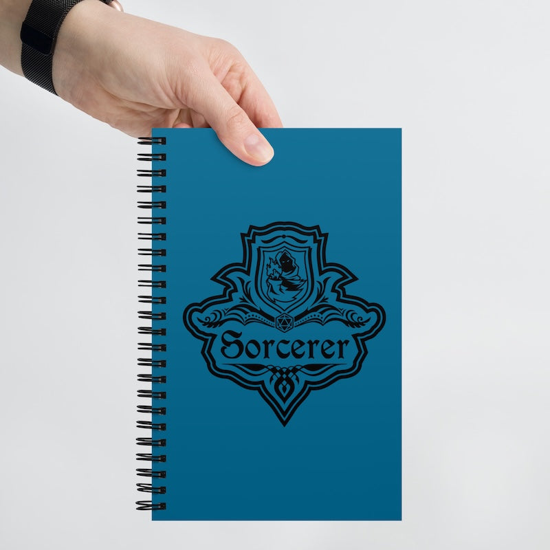 Blue notebook with 'Sorcerer' design held by a hand on a light gray background