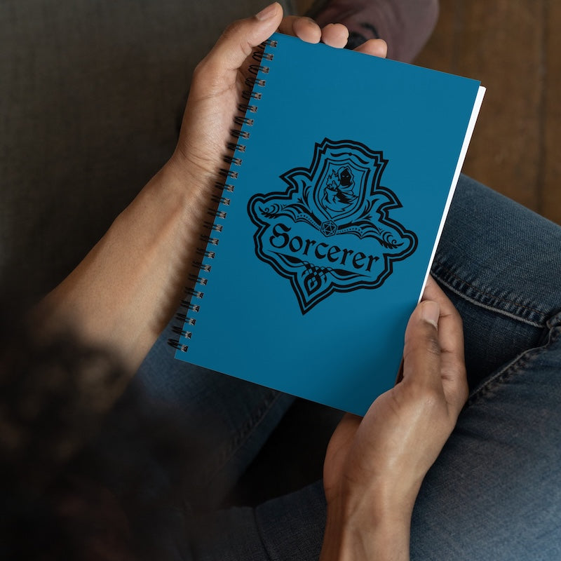 Blue notebook with 'Sorcerer' design held by a person sitting on a wooden floor.