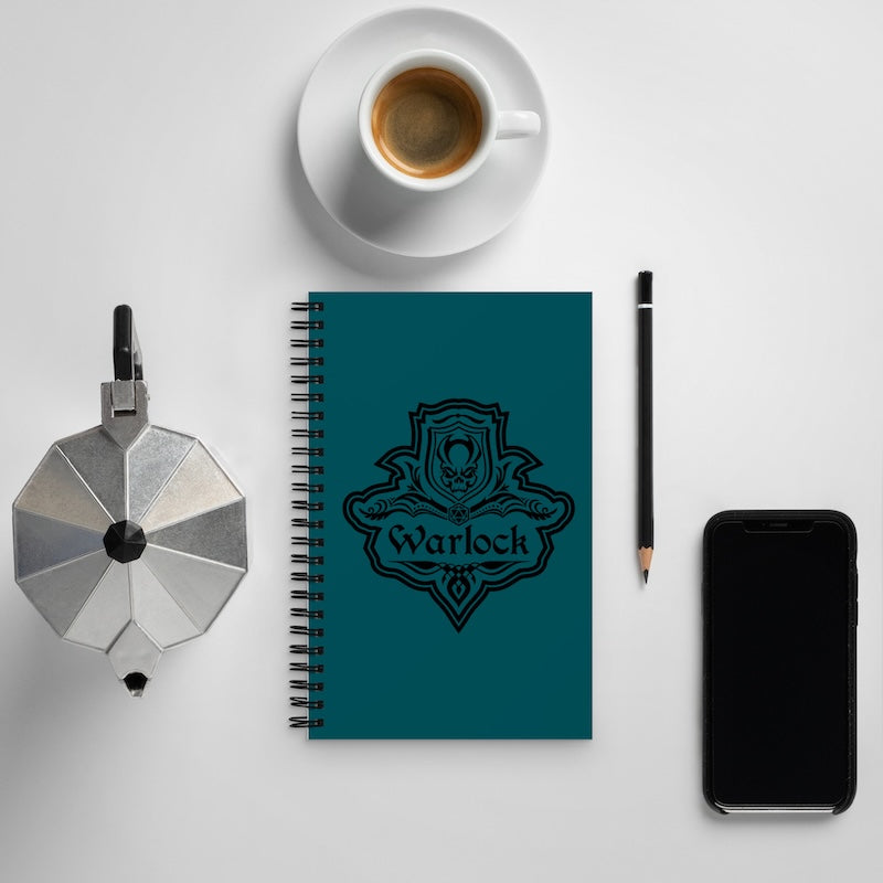 Teal notebook with 'Warlock' design, coffee cup, pencil, and phone on a light gray background