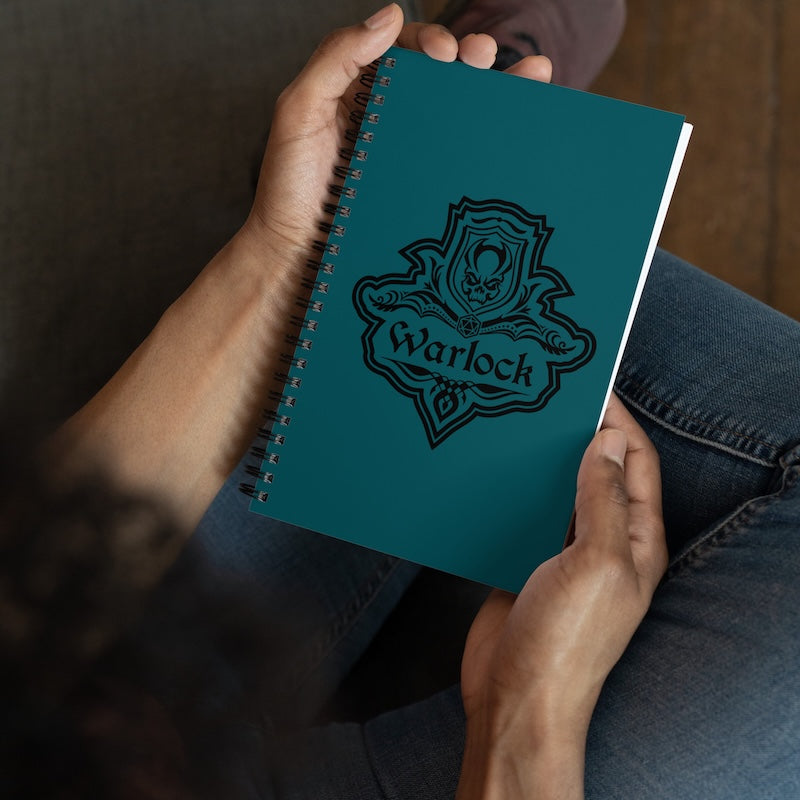 Teal notebook with 'Warlock' design held by a person wearing jeans.