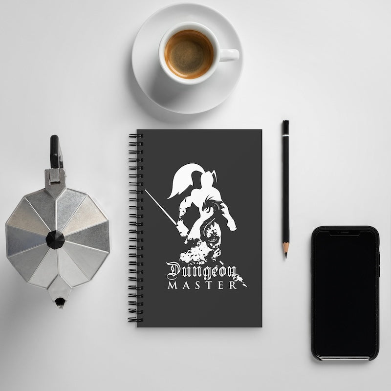 Notebook with 'Dungeon Master' design, coffee cup, phone, and pen on a light gray background