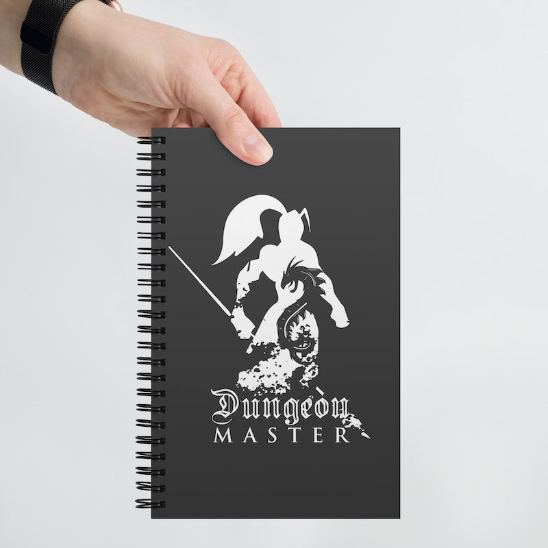 Black notebook with 'Dungeon Master' design held by a hand on a light gray background