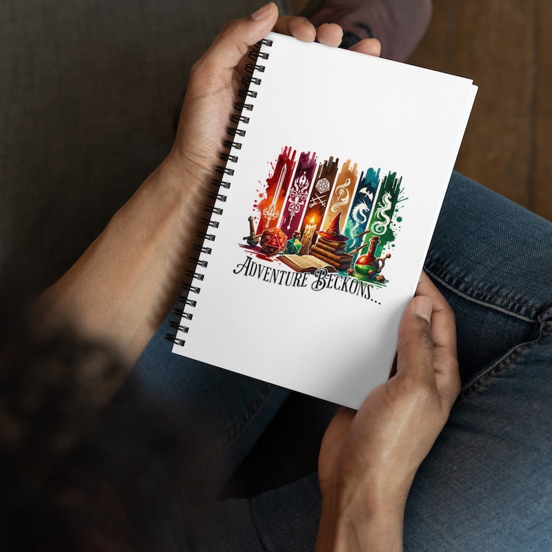 Person holding a notebook with 'Adventure beckons' design on the cover