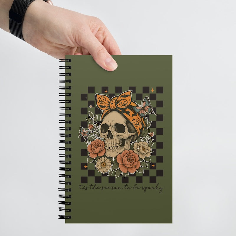 Notebook with skull and floral design held by a hand on a light gray background