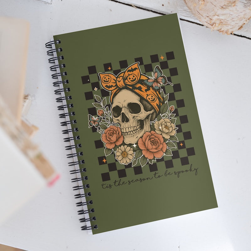 Green notebook with a skull and floral design on a white surface