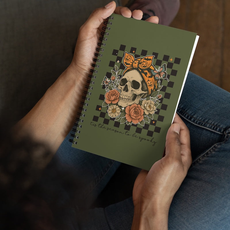 Green notebook with skull and floral design held by a person