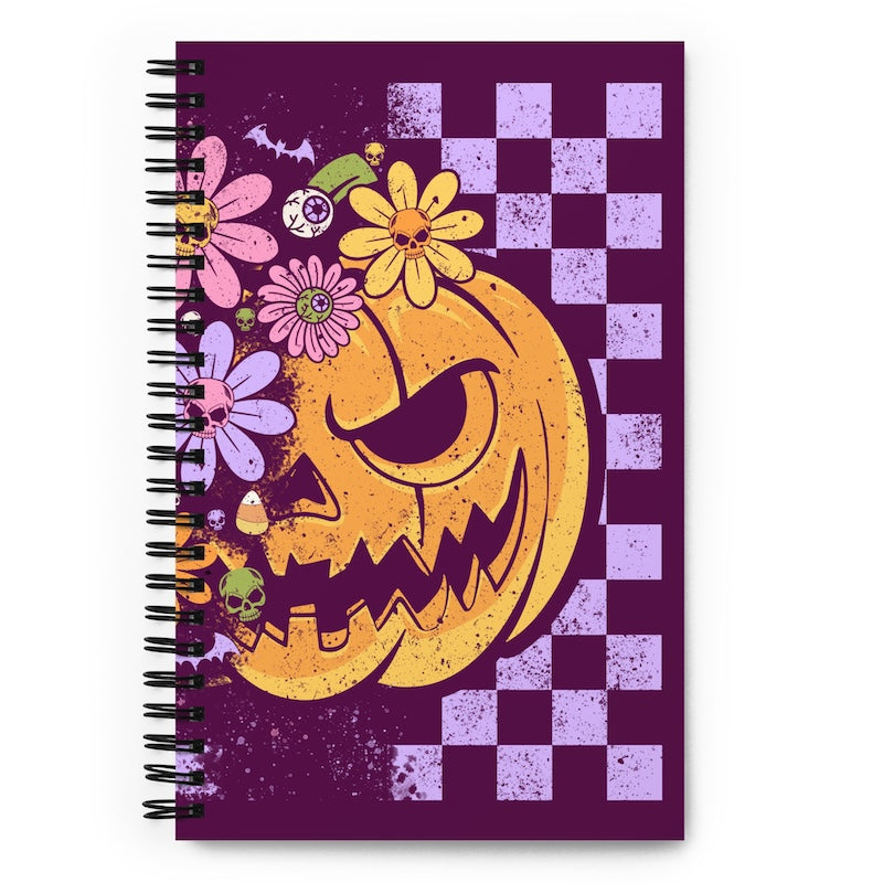 Notebook with a Halloween-themed design featuring a jack-o'-lantern face and flowers on a purple and checkered pattern background.