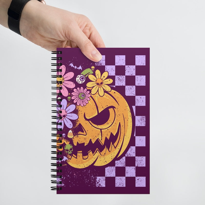 Notebook with Halloween design featuring a pumpkin and flowers held by a hand on a white background