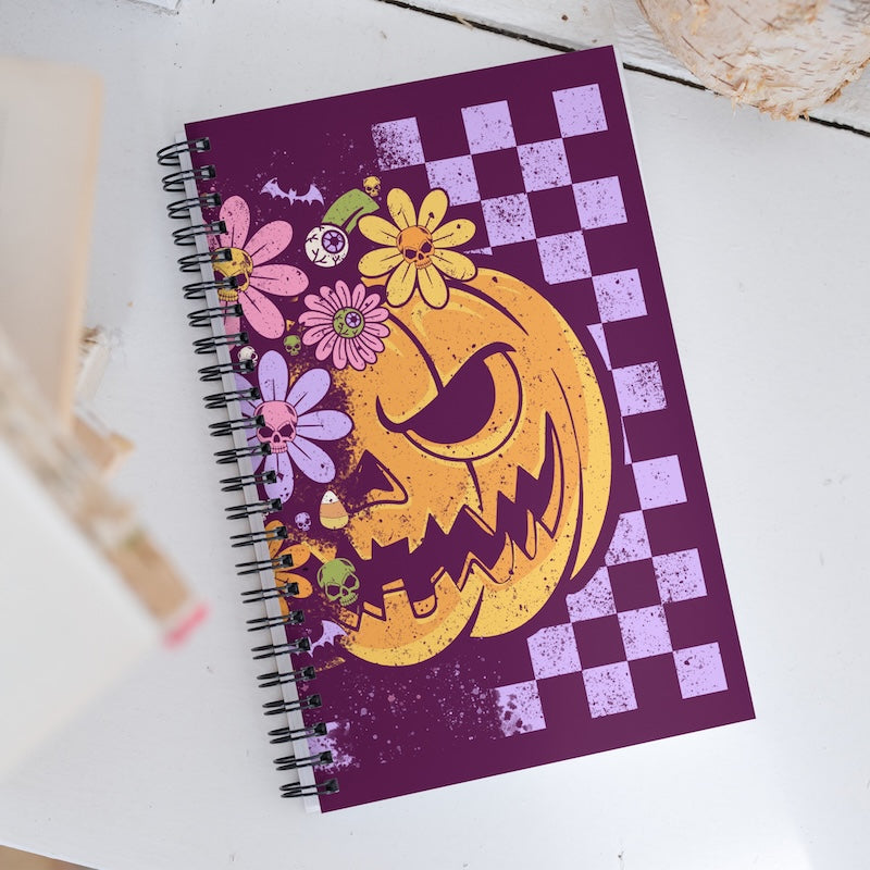 Notebook with a Halloween-themed design featuring a jack-o'-lantern and flowers on a purple background.