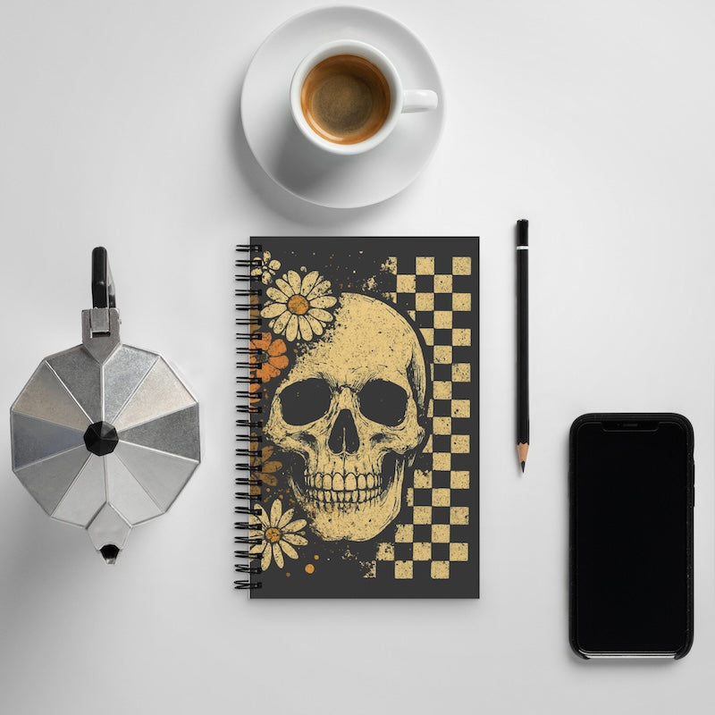 Notebook with skull design, coffee cup, phone, and other items on a light gray background