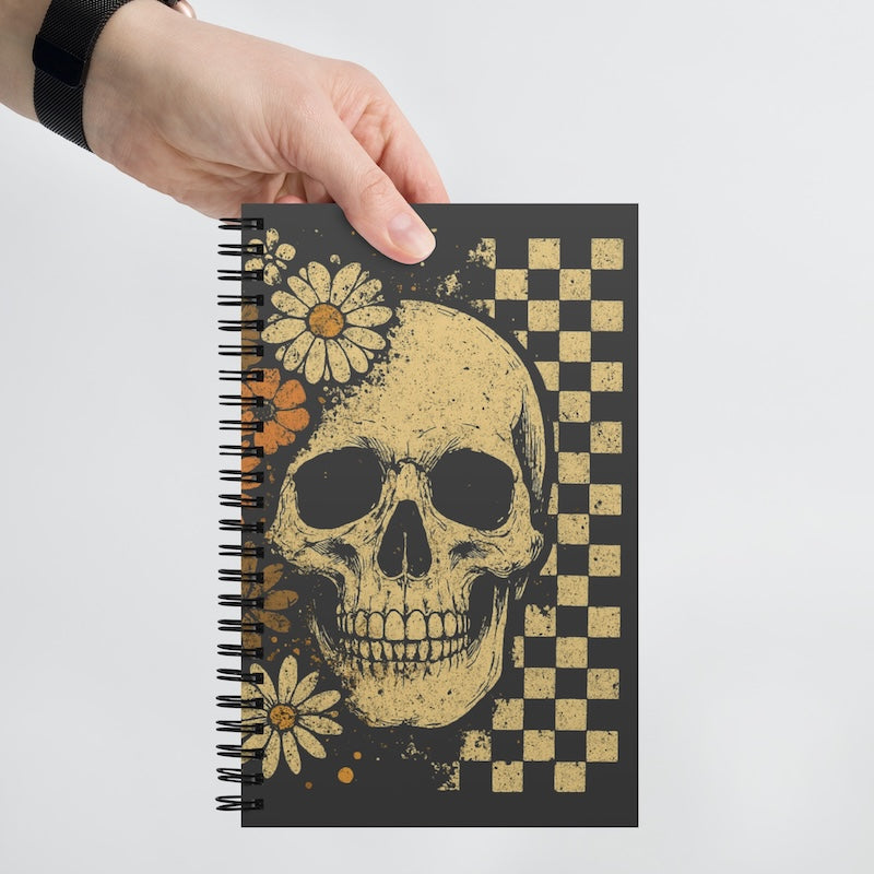 Notebook with skull and floral design held by a hand on a light gray background